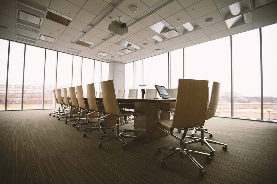 An empty boardroom with a long table and city light through the windows